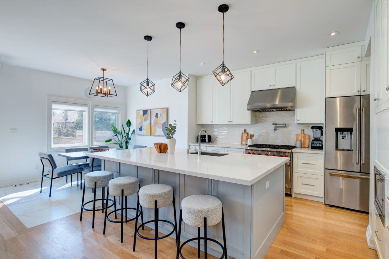 stunning kitchen designed with modern elements, stools lined up at a large island and a big bright window looking out over the backyard.